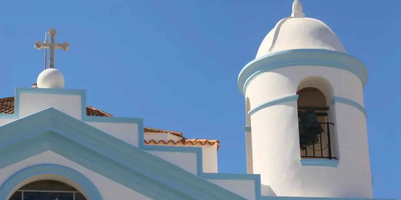Campanile e croce su edificio bianco con dettagli azzurri, nel cuore del calasetta centro storico.