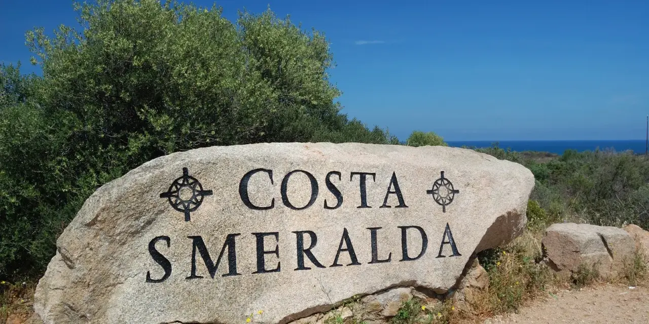 Masso con scritta "COSTA SMERALDA" in Sardegna, dove il mare azzurro incontra la macchia mediterranea.
