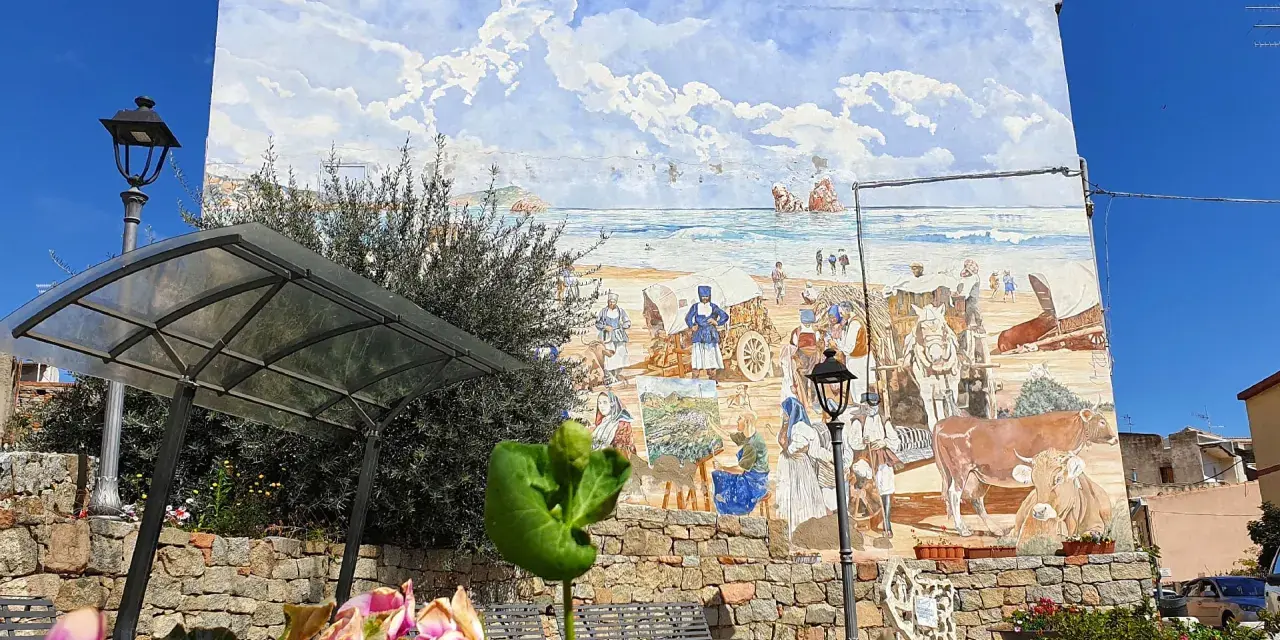 Un murale colorato a Loceri, Sardegna, raffigura scene di vita marina e rurale con persone, carri e animali sotto un cielo azzurro e nuvoloso.