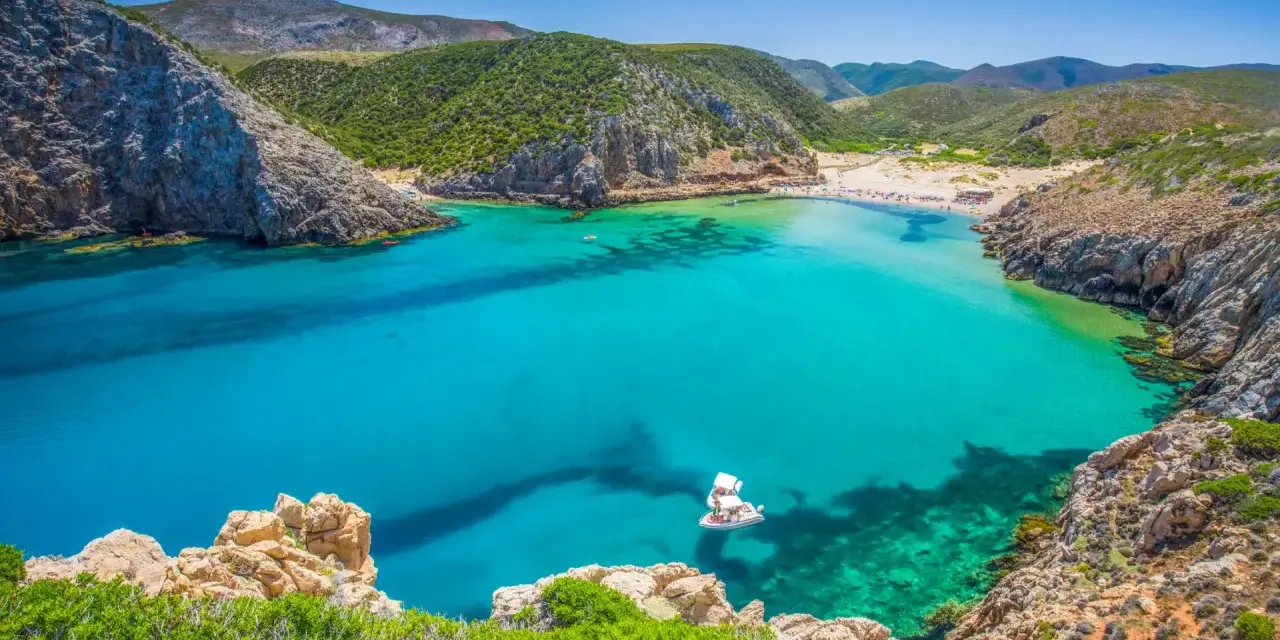 La splendida spiaggia di Buggerru, con acque cristalline e rocce imponenti, invita al relax. Una barca bianca solca il mare turchese.