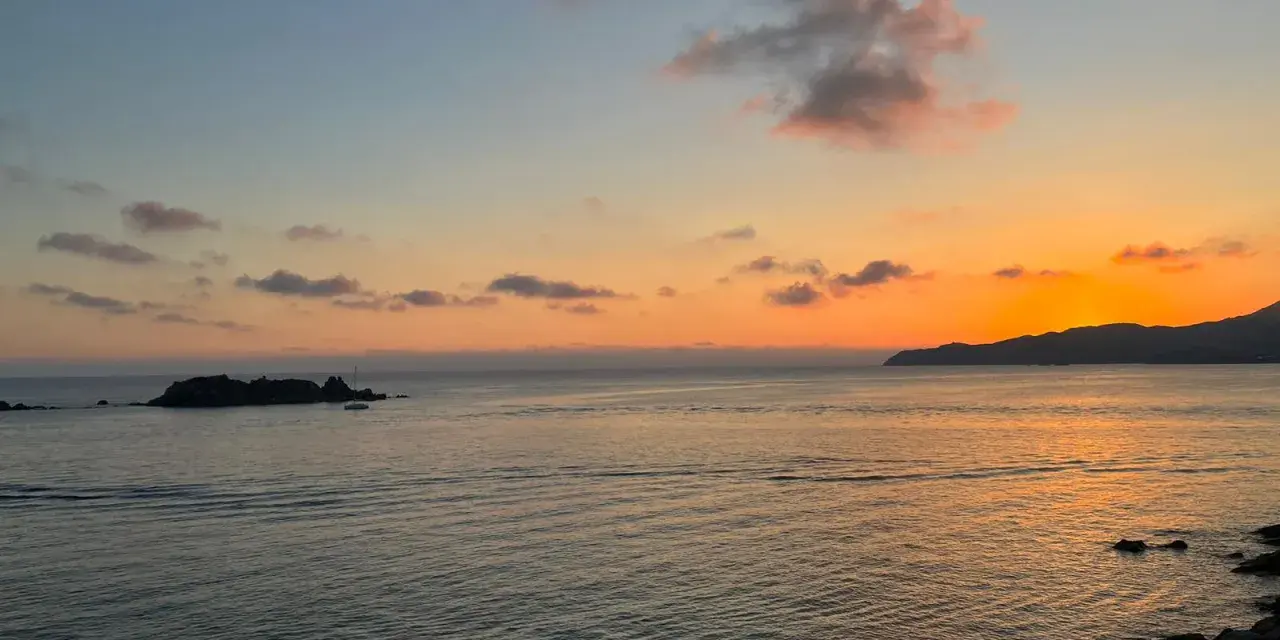 Un tramonto mozzafiato sul mare, con un'isola rocciosa e una barca a vela. Un luogo perfetto per ammirare dove vedere il tramonto a Villasimius.
