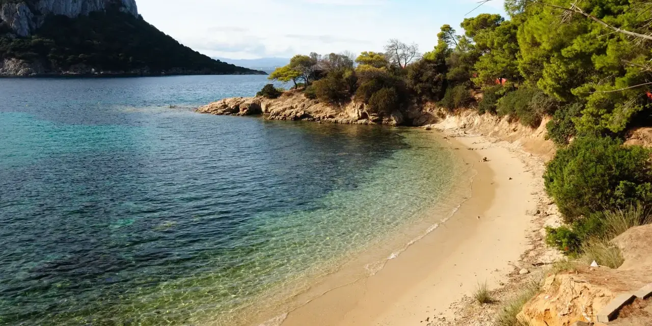Spiaggia dorata e acque cristalline nella baia di Cala Moresca, con una scogliera verdeggiante e un promontorio roccioso sullo sfondo.