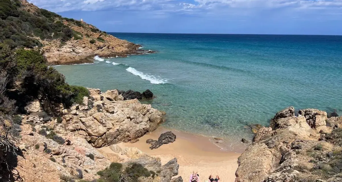 Spiaggia selvaggia vicino al centro storico di Chia, con rocce dorate, mare cristallino e due persone che prendono il sole.