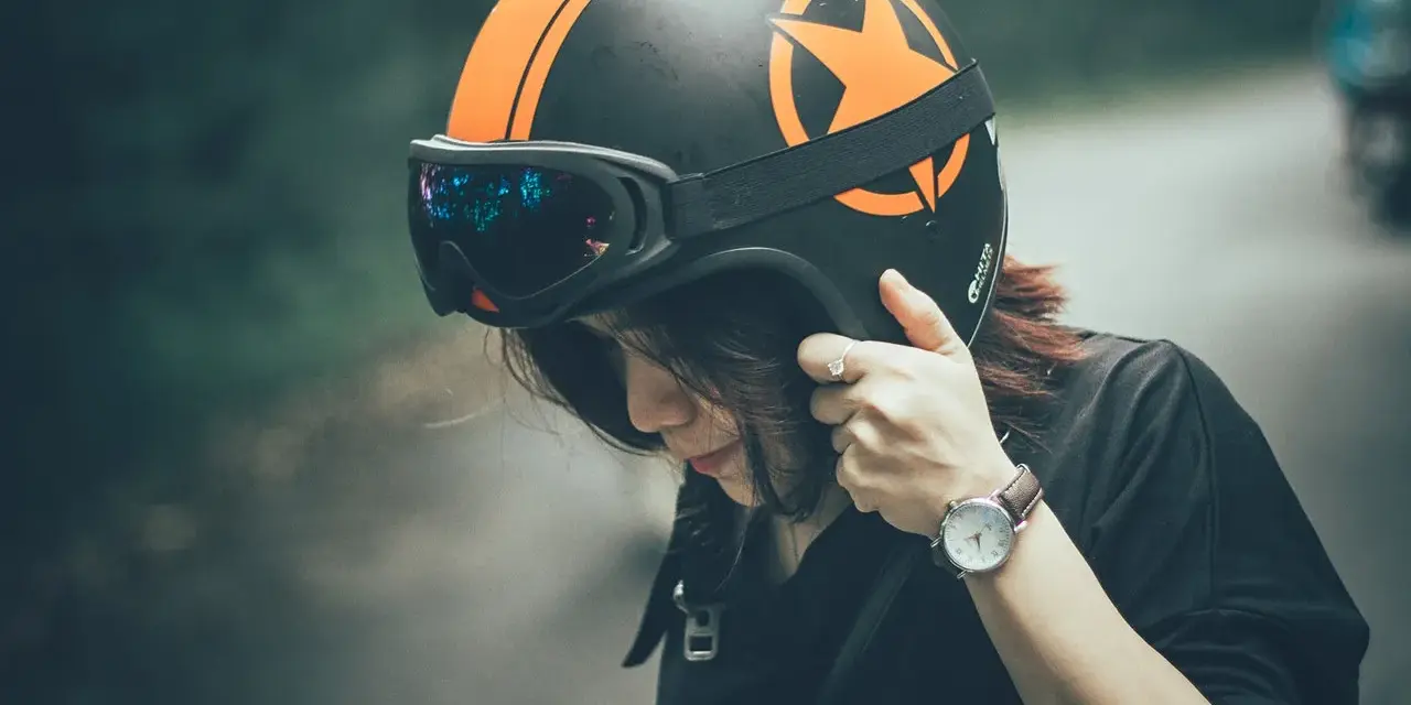 Ragazza con casco moto nero e arancione, occhiali vintage. Guida sicura: come scegliere casco moto.