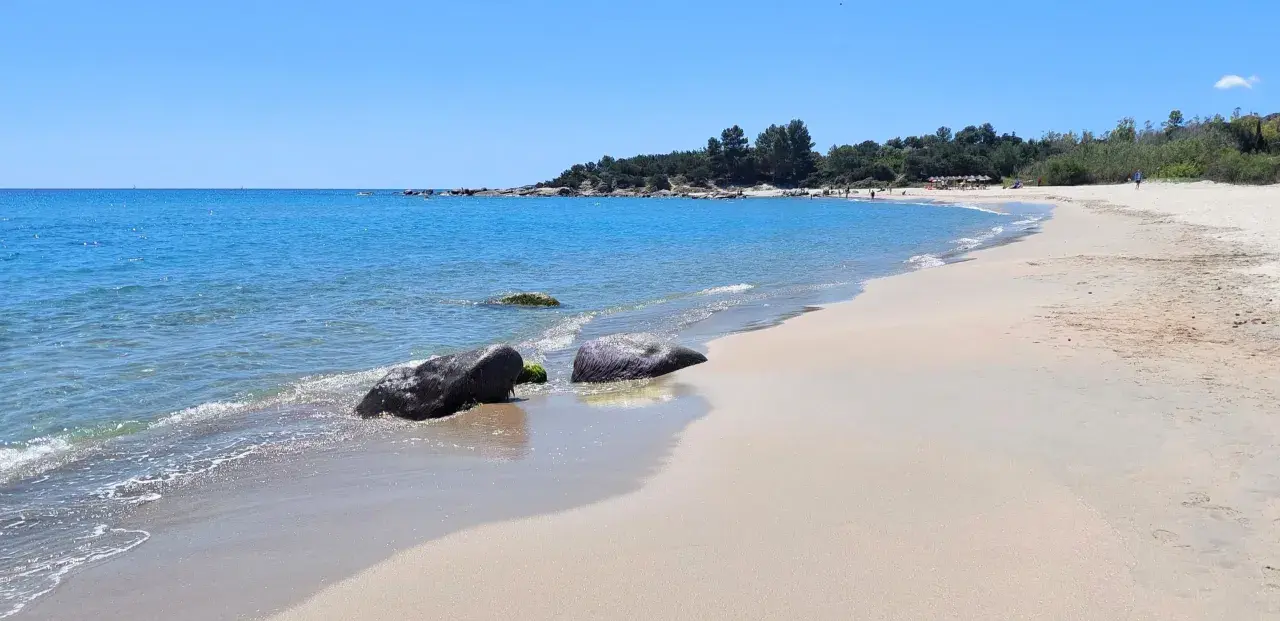 Spiaggia di Lido di Orrì con rocce scure bagnate dall'acqua cristallina e sabbia dorata.