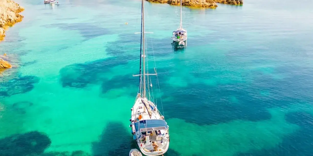 Vela al largo di Cala Ambra, con acque cristalline e un paesaggio roccioso.