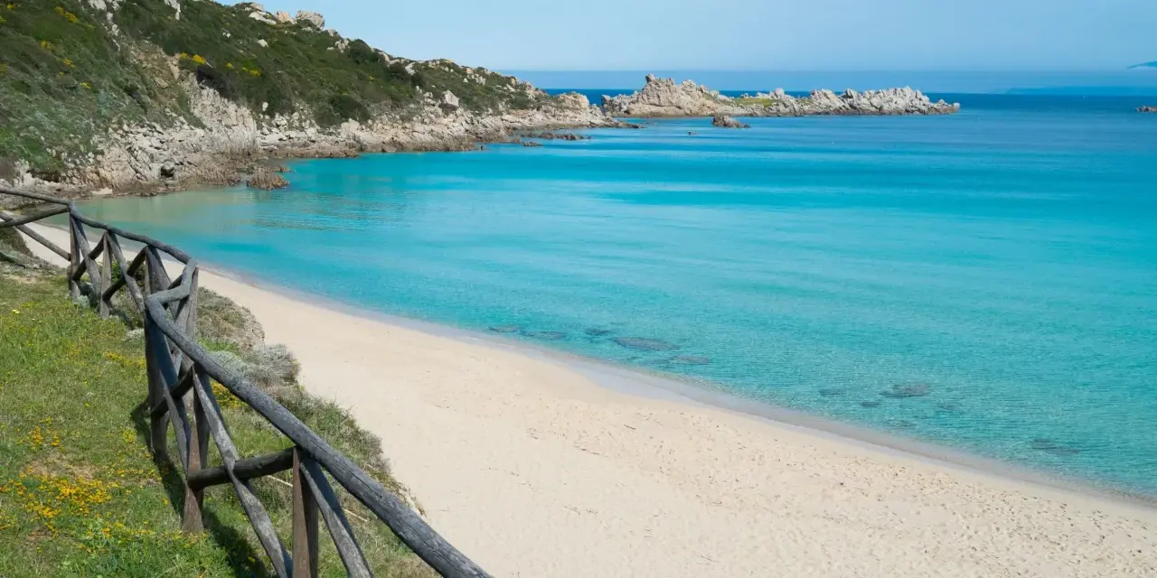 Una splendida spiaggia rena bianca bagnata da un mare cristallino. La vegetazione mediterranea e le rocce scolpite dal vento completano il paesaggio.