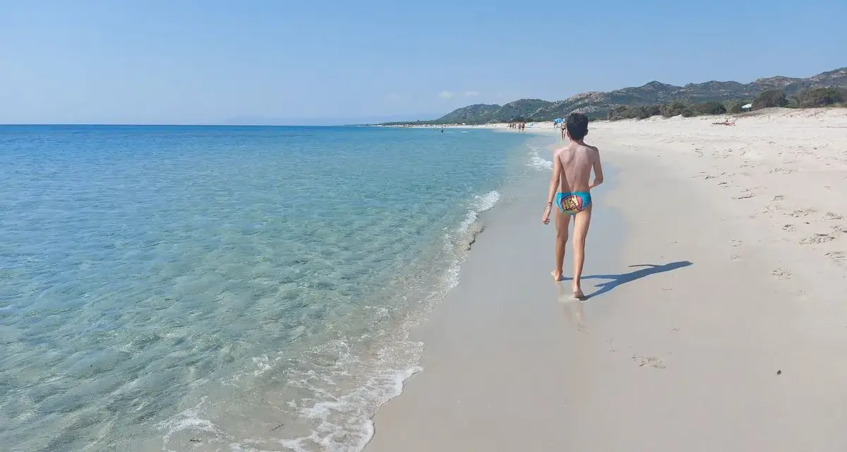 Bambino cammina su una delle splendide spiagge della costa est della Sardegna, con mare cristallino e sabbia bianca.