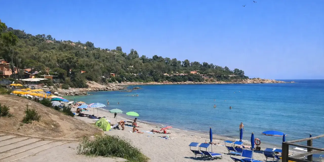 Spiaggia di Porto Frailis con ombrelloni colorati, lettini blu e gente che si gode il mare cristallino sotto il sole.