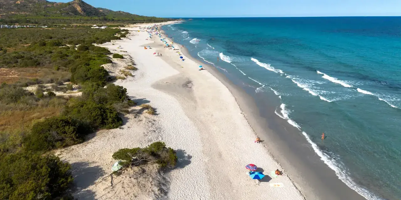 L'oasi di Bidderosa, una spiaggia sarda con sabbia chiara, vegetazione mediterranea e mare turchese, accoglie bagnanti sotto ombrelloni colorati.