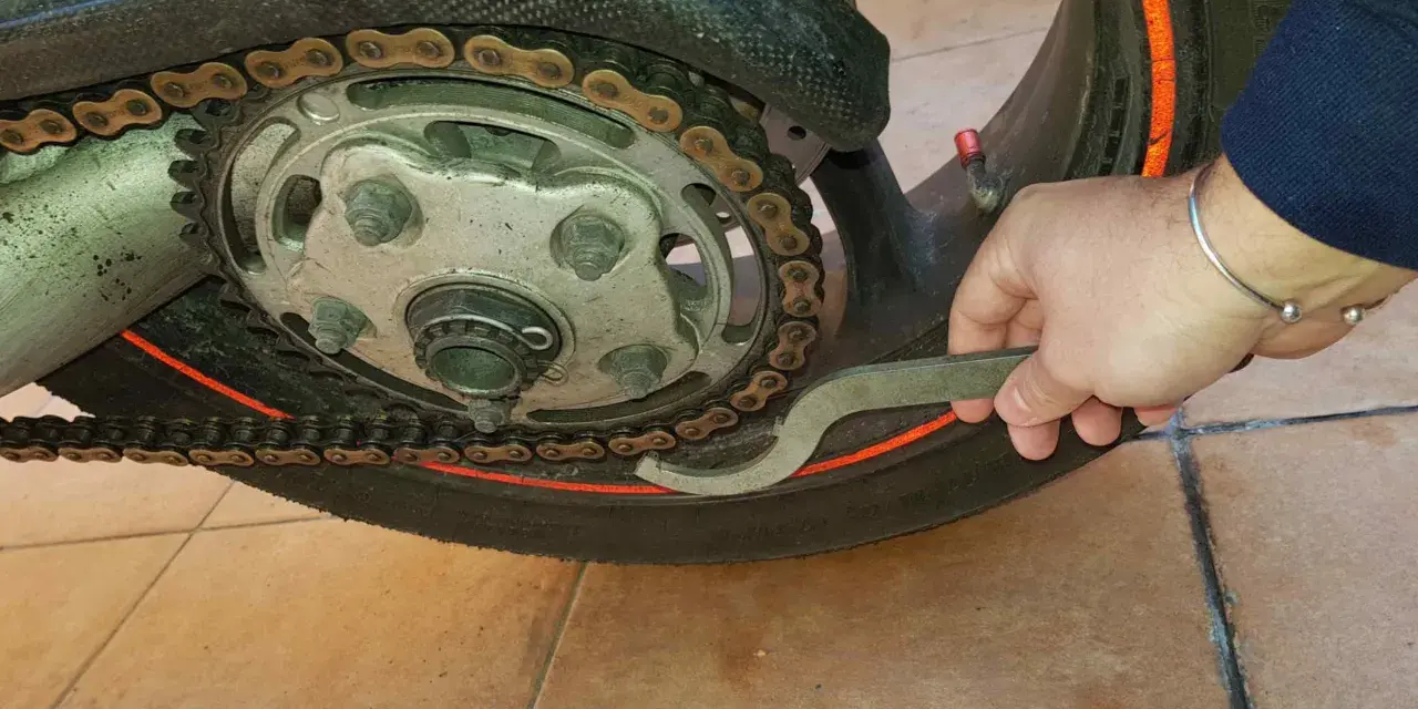 Mano con chiave inglese che lavora sulla catena di una moto, mostrando come tirare la catena della moto per la manutenzione.