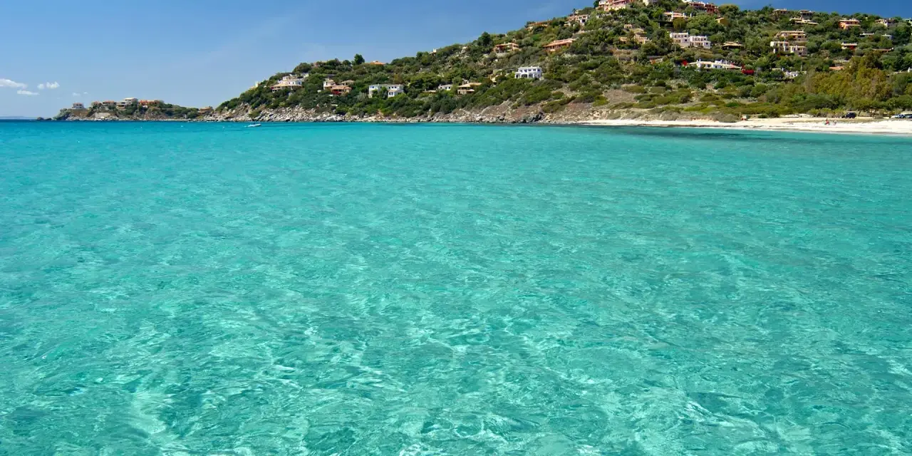 Acque cristalline e una collina verdeggiante punteggiata di case bianche e rosse, con la **spiaggia Torre delle Stelle** che si estende in lontananza.
