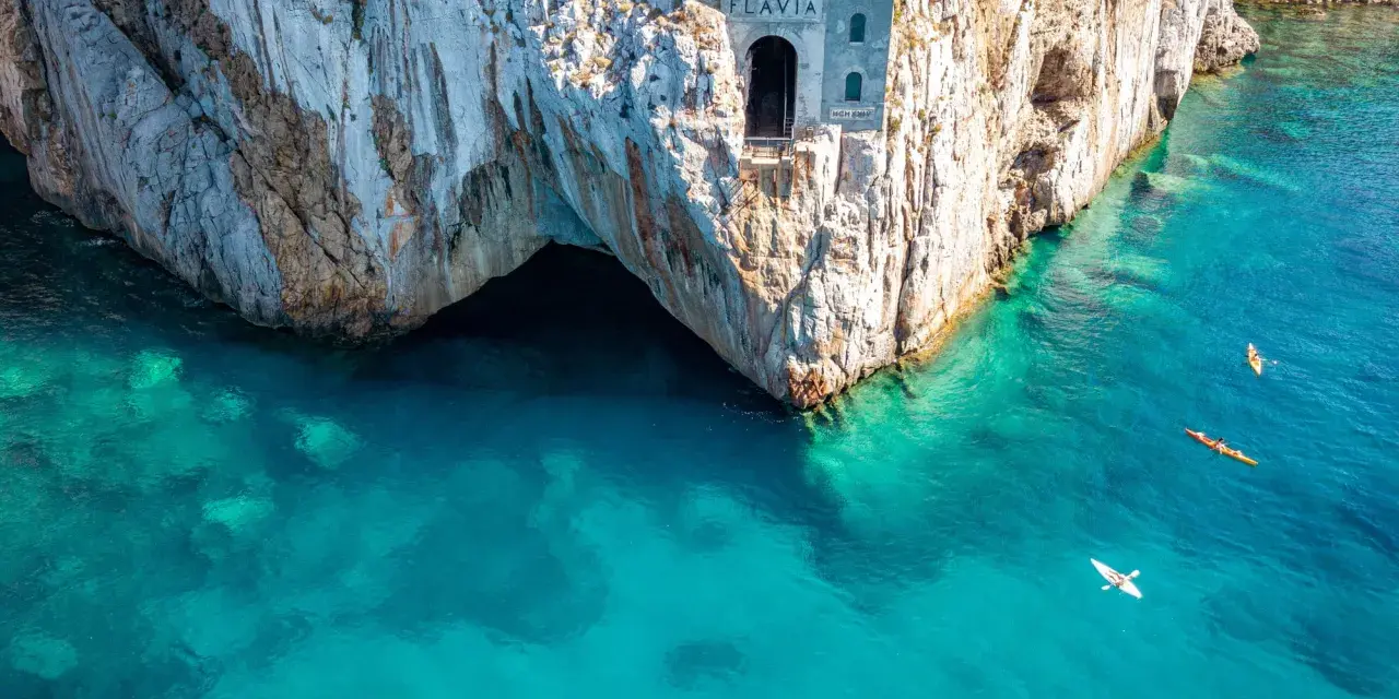 Porto Flavia, un'antica struttura legata alle miniere abbandonate della Sardegna, si affaccia su un mare cristallino. Kayak solcano le acque turchesi.