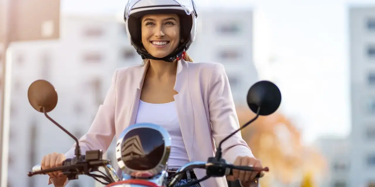 Donna sorridente in motorino, con casco bianco, rispetta l'obbligo casco motorino per la sua sicurezza.