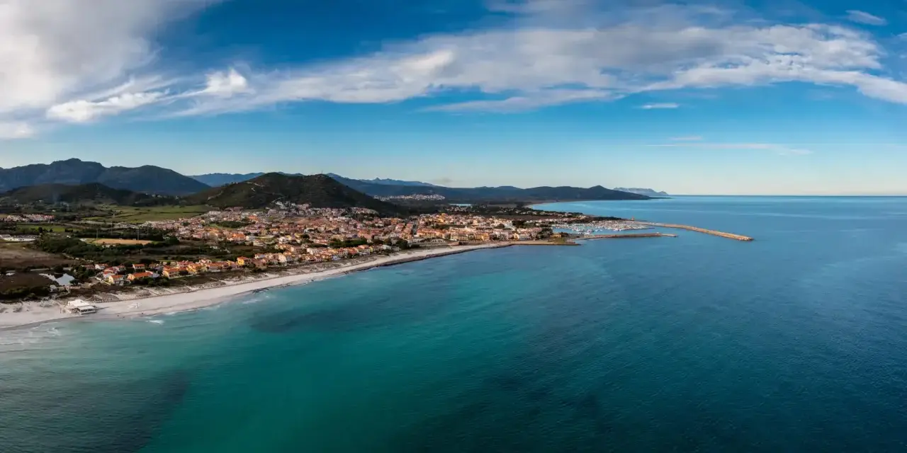 Vista aerea di Posada, Siniscola, con la sua spiaggia dorata, il mare turchese e le case colorate che si affacciano sulla costa.