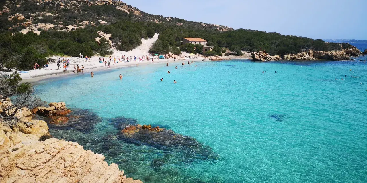 La **cala Granara** splende con acque cristalline e una spiaggia affollata di bagnanti. Rocce dorate emergono dal mare turchese.