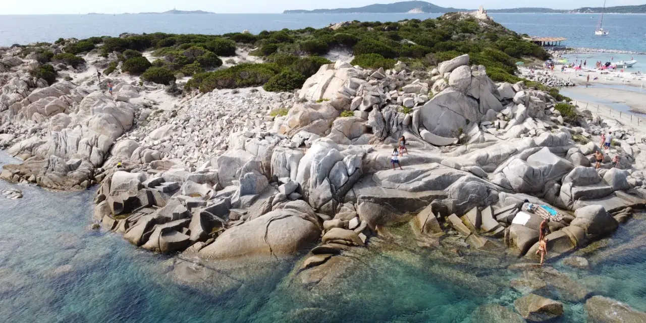 Scogliere rocciose e acque cristalline sulle spiagge a Villasimius. Turisti esplorano la costa selvaggia e si godono il sole.