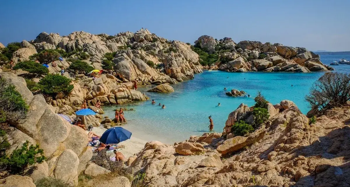 Una baia con rocce granitiche scolpite dal vento e acque turchesi cristalline, tra le spiagge più belle sardegna nord. Gente rilassata sotto gli ombrelloni.