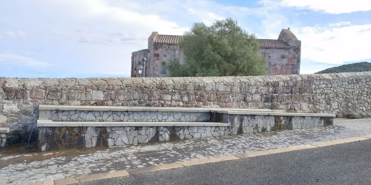 Fontana in pietra con scorci di un antico edificio religioso, un'oasi di pace ad **Allai, Sardegna**.