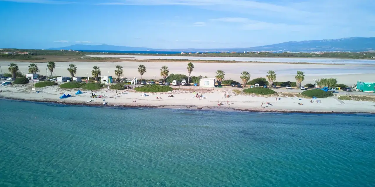 Spiaggia di Putzu Idu con palme, camper e gente che si gode il sole. Acqua cristallina e cielo azzurro.