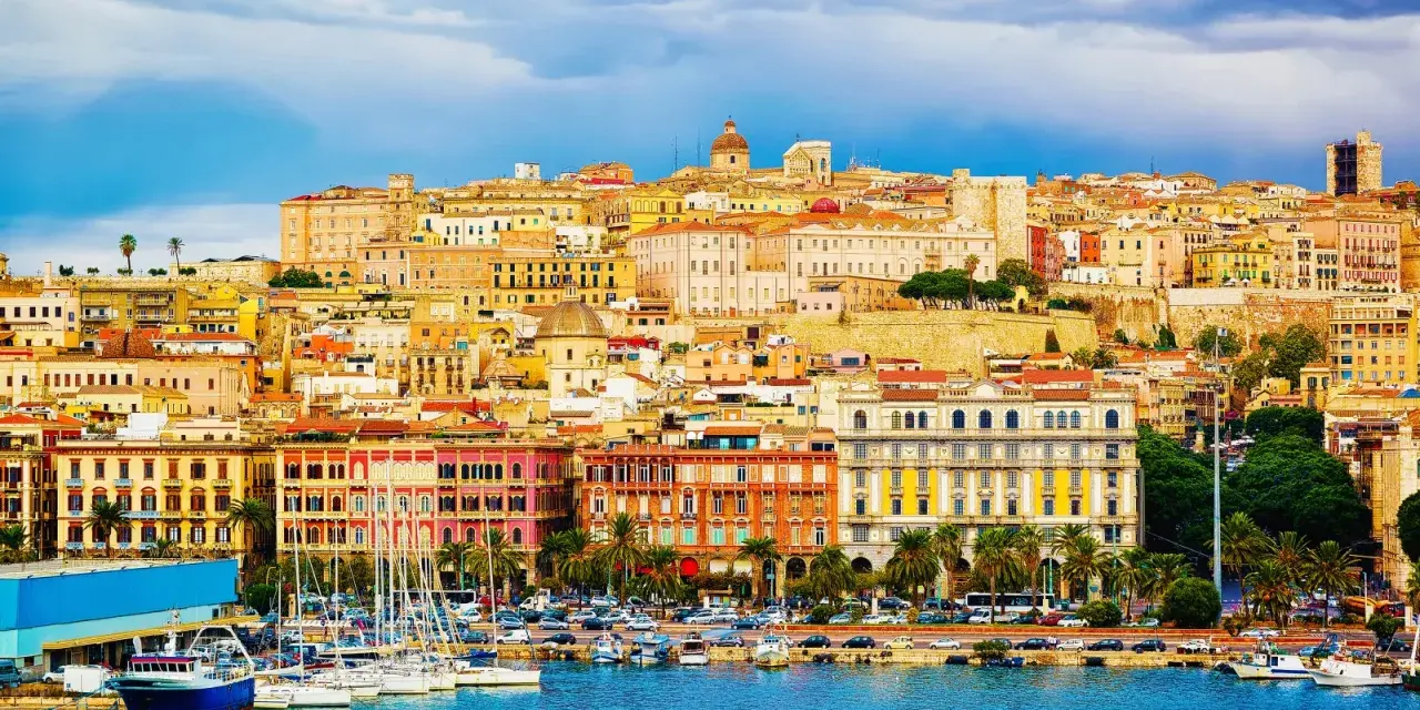 Panoramica colorata di **Mirrionis**, con edifici storici, un porto con barche a vela e un cielo azzurro con nuvole.
