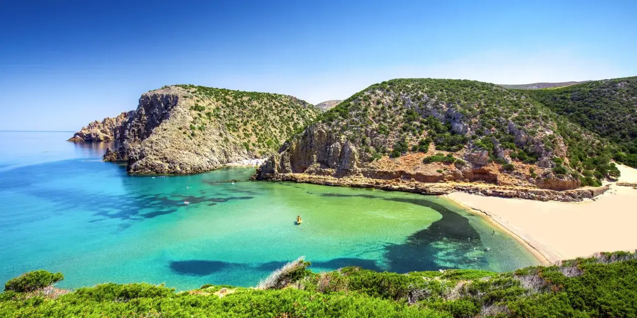 Baia con acque cristalline e sabbia dorata, incastonata tra scogliere verdi. Un vero gioiello tra le spiagge più belle in Sardegna.