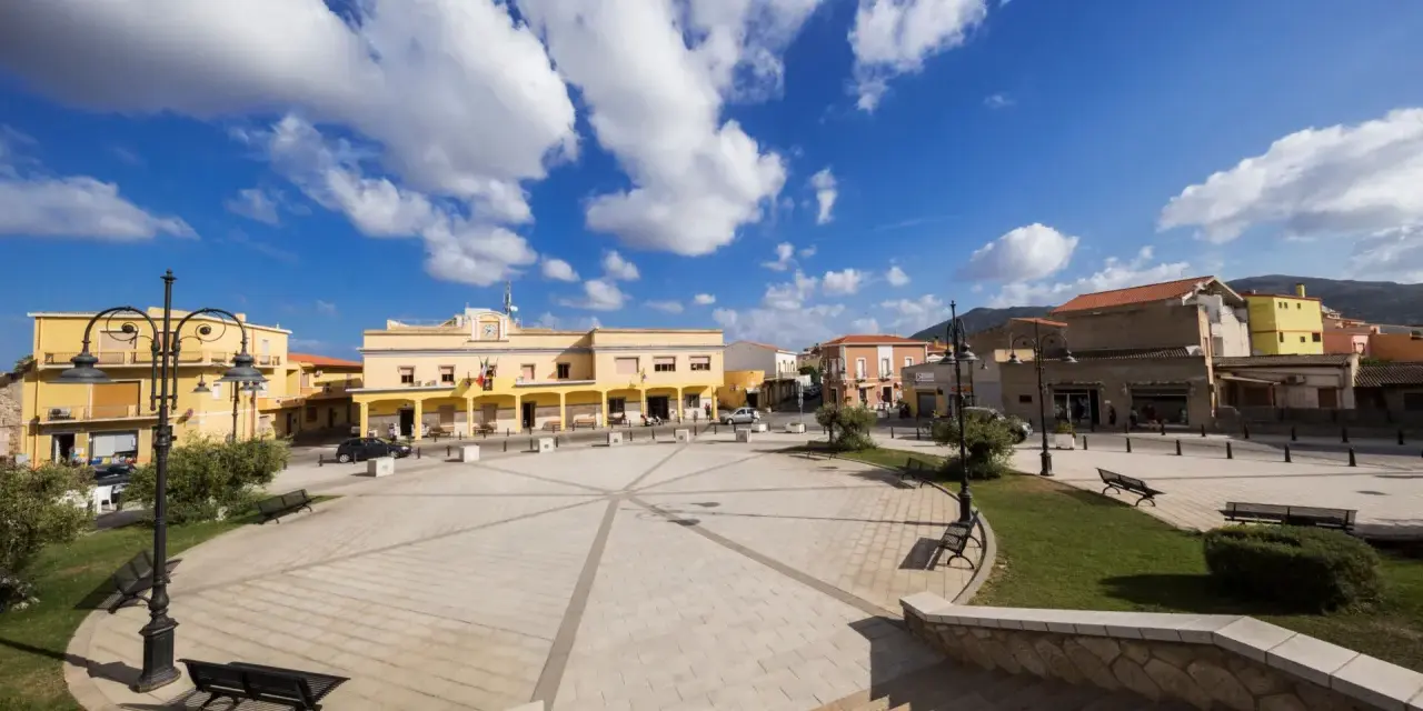 Piazza di San Giovanni Suergiu con edifici gialli e cielo azzurro.