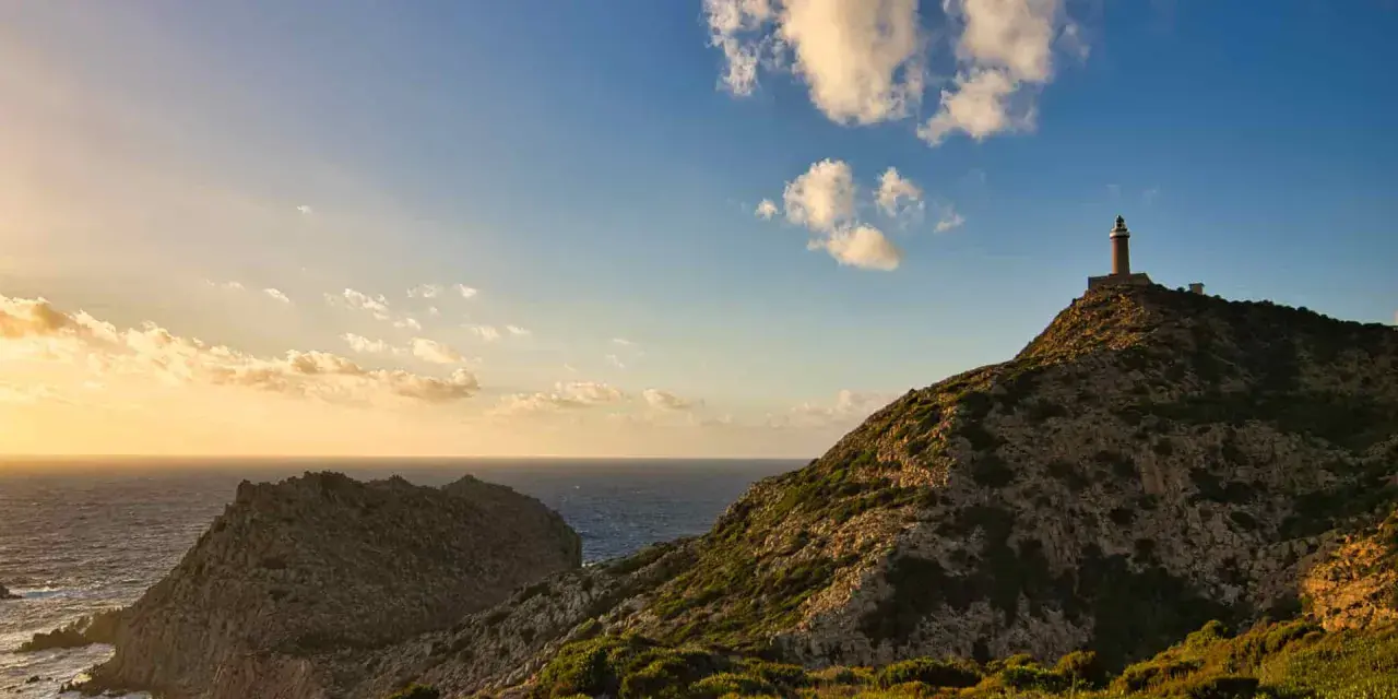 Faro solitario su una collina rocciosa, con il mare e le nuvole al tramonto. Un paesaggio mozzafiato di Nebida, Sardegna.