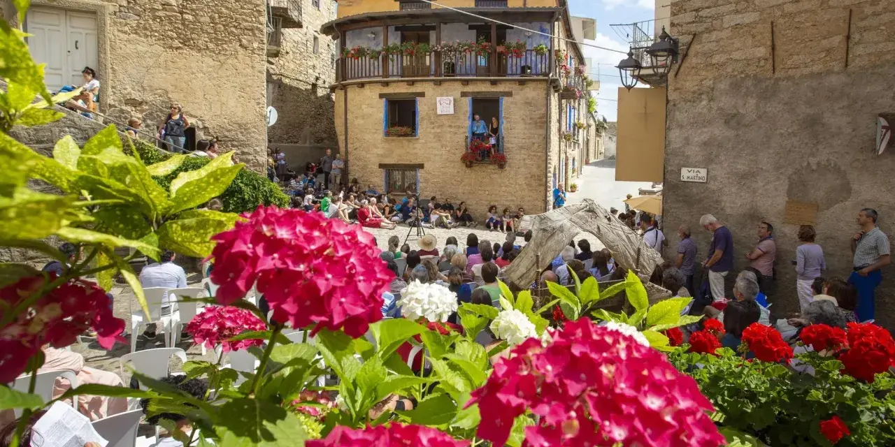 Fiori rosa e bianchi incorniciano una piazza con gente seduta, in attesa di uno spettacolo. Un evento da non perdere, ecco **gavoi cosa vedere**!