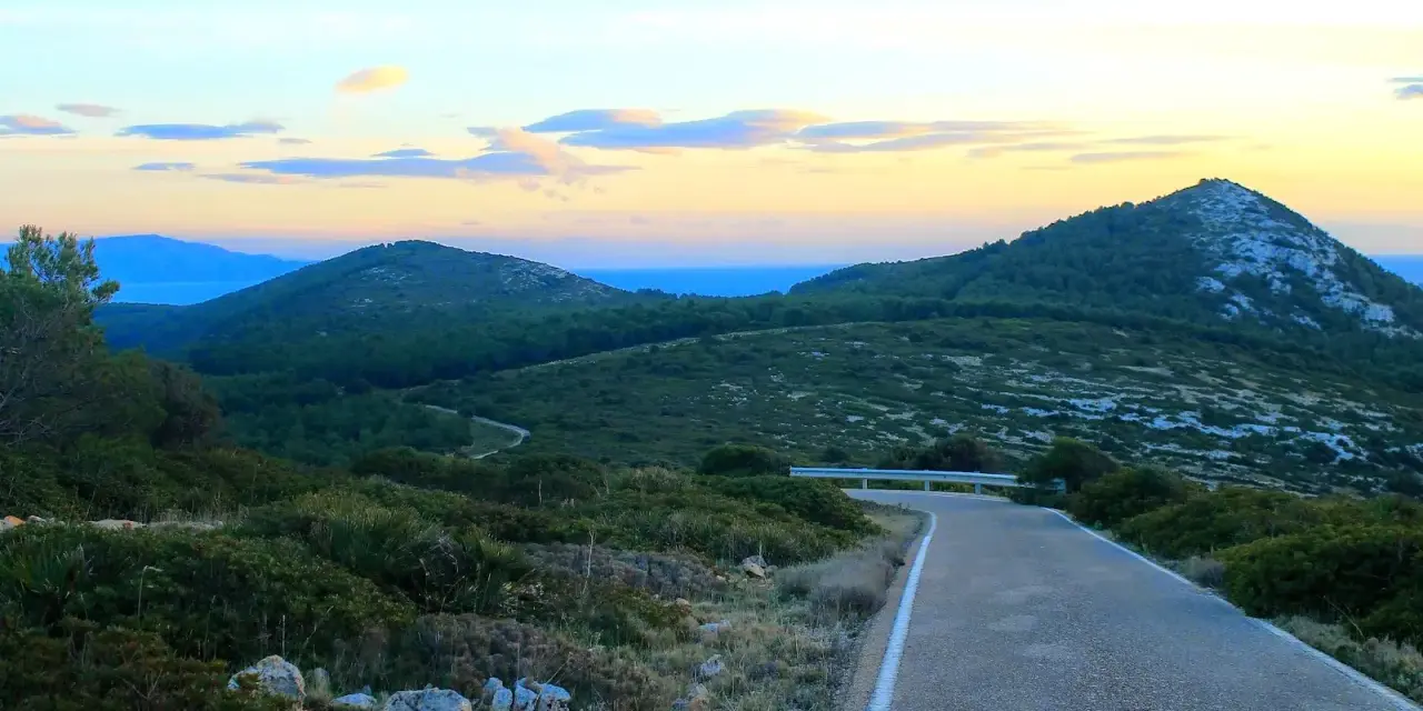 Strada panoramica verso il monte Doglia al tramonto, con colline verdi e cielo colorato.