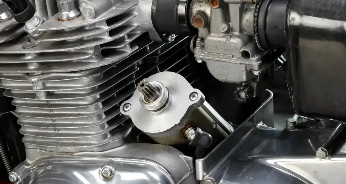 Dettaglio del motore di una moto: il test del motorino di avviamento è in primo piano, con il carburatore e le alette di raffreddamento visibili.