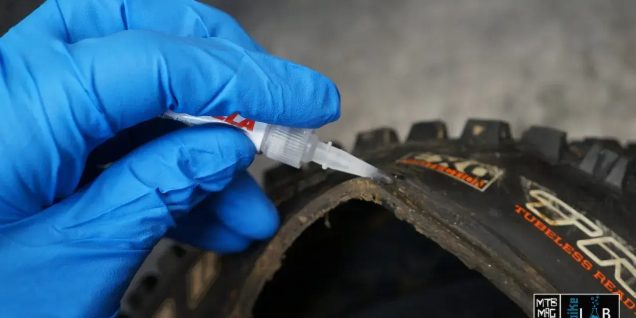 Mano con guanto blu applica colla per pneumatici tubeless riparazione su un copertone da MTB.
