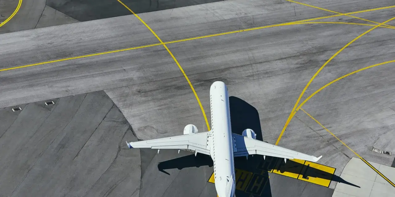 Aereo bianco in attesa sulla pista di uno degli aeroporti della Sardegna, con segnaletica gialla che guida il traffico aereo.
