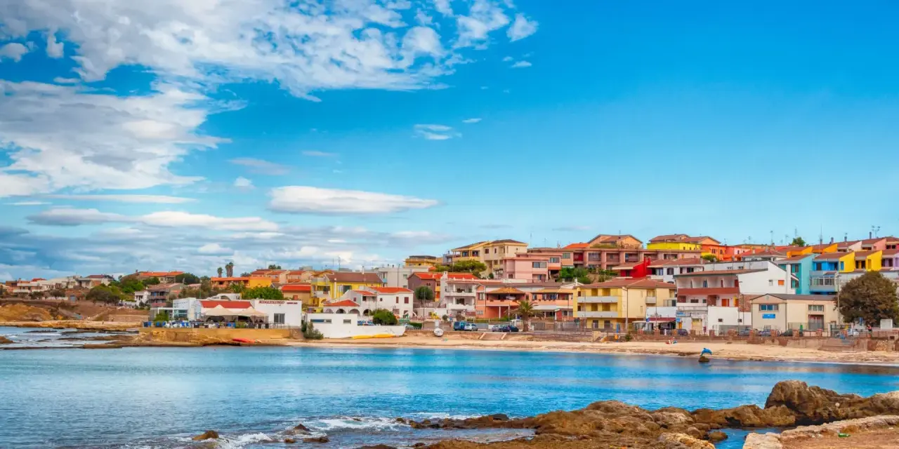 Colorate case affacciate sul mare blu, con rocce in primo piano. Il centro storico di Porto Torres, un incanto sardo.