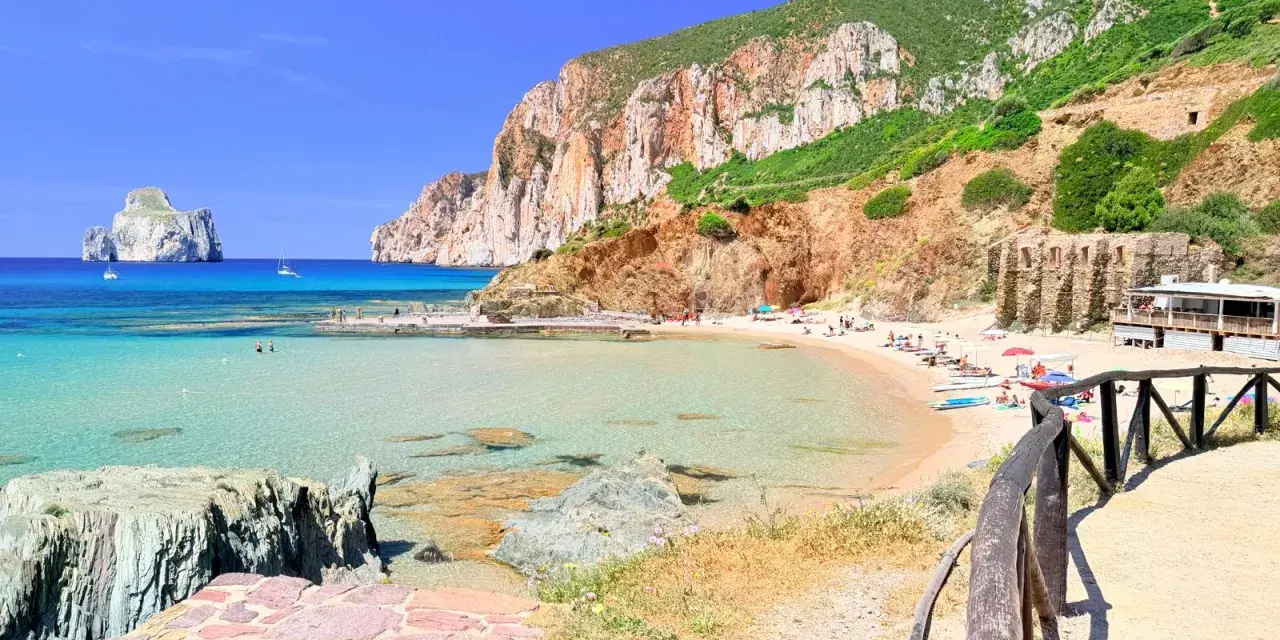 Spiaggia di Masua con acque cristalline, scogliere imponenti e il Pan di Zucchero all'orizzonte. Relax e natura incontaminata.