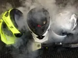 Tre caschi, uno giallo fluo, uno bianco e nero, e uno bianco, sono avvolti dal vapore. Un accessorio per la pulizia a vapore è posizionato davanti a loro, suggerendo che il casco non deve essere pulito con solventi.