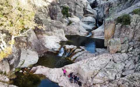 Un gruppo di escursionisti ammira un canyon con cascate e pozze d'acqua cristallina. Uno di loro, con un giubbotto rosa acceso, sembra dire "bau mela!" alla natura.