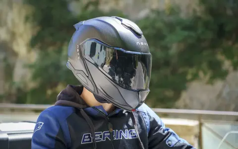 Casco da moto nero con visiera riflettente, che offre una sensazione di pressione sulla fronte. Indossato da una persona con giacca blu e nera.
