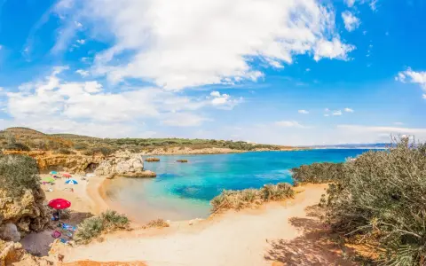 Spiaggia Lazzaretto ad Alghero: sabbia dorata, acque cristalline e macchia mediterranea sotto un cielo azzurro con nuvole bianche.