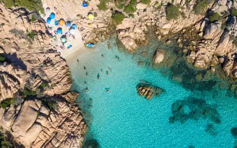 Vista aerea della spiaggia di Cala Coticcio, con bagnanti che si godono le acque cristalline e ombrelloni colorati sulla sabbia dorata.