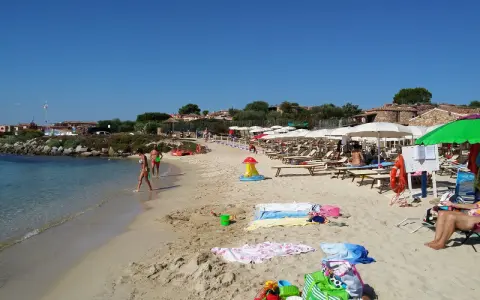 A sunny beach with people walking in the shallow water and lounging under umbrellas.