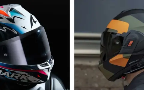 Due caschi da moto, uno bianco con grafiche colorate e il logo Shark, l'altro nero con mimetica arancione e verde. Essenziali protezioni obbligatorie moto.