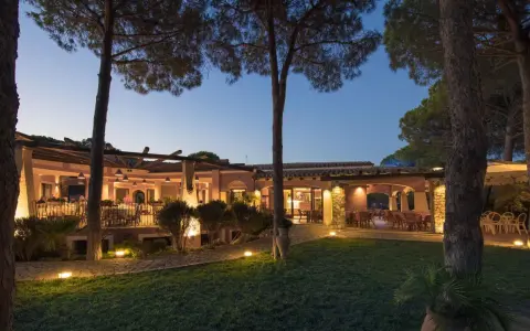La sorgente Villasimius: un ristorante con tavoli all'aperto illuminati da luci soffuse, circondato da pini e un prato curato.