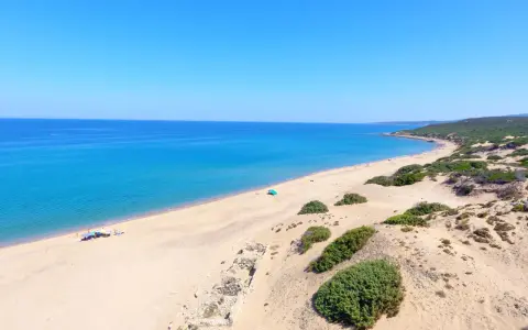 Vasta spiaggia di sabbia dorata, mare azzurro e vegetazione mediterranea sulla spiaggia di Piscinas. Rovine antiche emergono dalla sabbia.