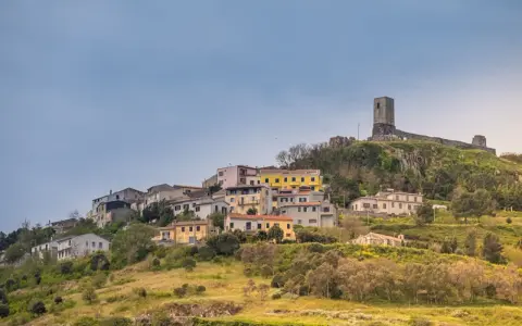 Il castello di Osilo domina un borgo colorato su una collina verdeggiante, sotto un cielo azzurro.