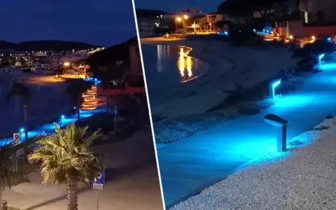 Passeggiata illuminata da luci blu sul lungomare di Golfo Aranci sera, con palme e case sullo sfondo.