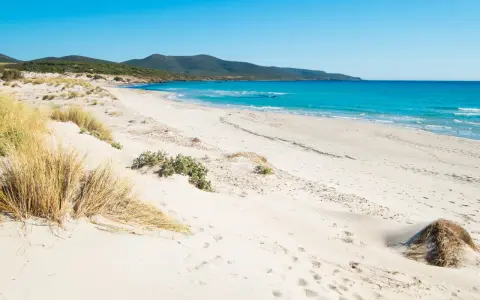 Spiaggia di Porto Pino con dune sabbiose e mare turchese sotto un cielo azzurro.