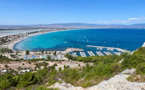 Vista panoramica della spiaggia del Poetto con mare turchese, porto turistico e saline rosa sullo sfondo.