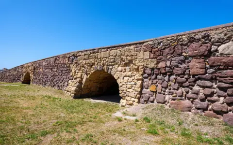 Antico ponte romano a Sant'Antioco, con archi in pietra e un muro imponente sotto un cielo azzurro.