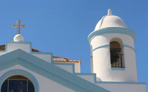 Campanile e croce su edificio bianco con dettagli azzurri, nel cuore del calasetta centro storico.